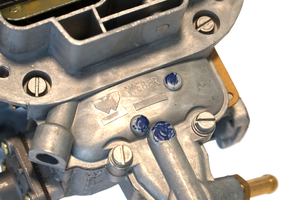 Close-up of a Weber carburetor with visible branding on a white background